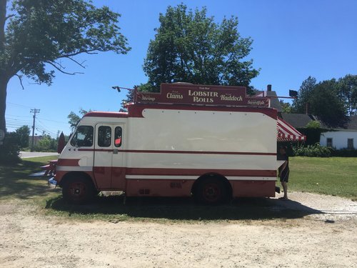 Red and white lobster roll food truck parked on gravel