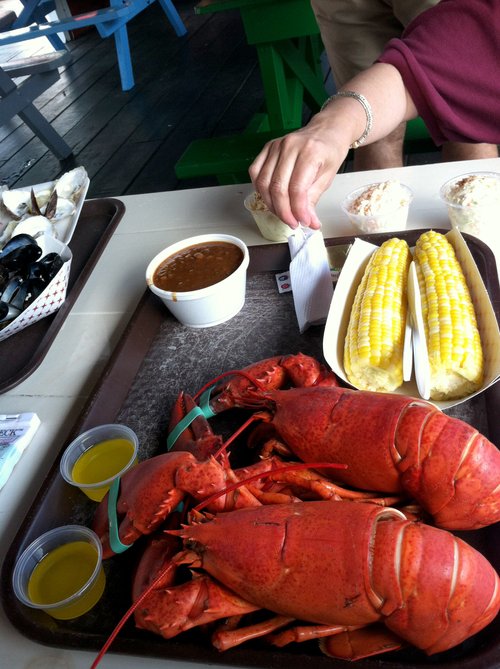 Boiled lobsters, corn on the cob, chowder and melted butter on a tray