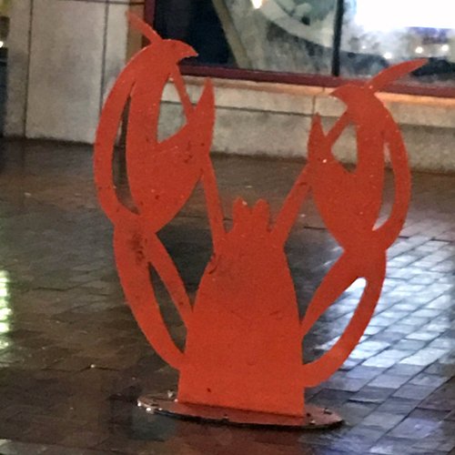 Red metal lobster cut-out sign on a sidewalk at night