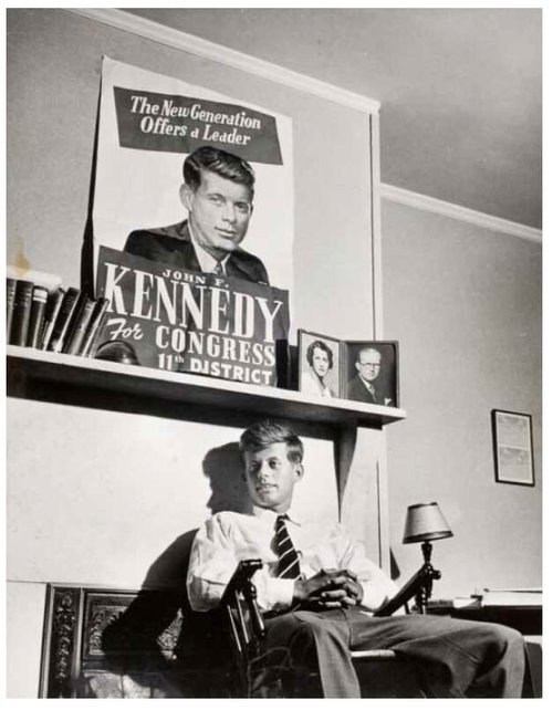 John F. Kennedy, age 29, sitting under a campaign poster in a room at the Bellevue Hotel during his 1946 campaign. On the mantle are photos of his parents. Photograph by Joel Yale for Life magazine.