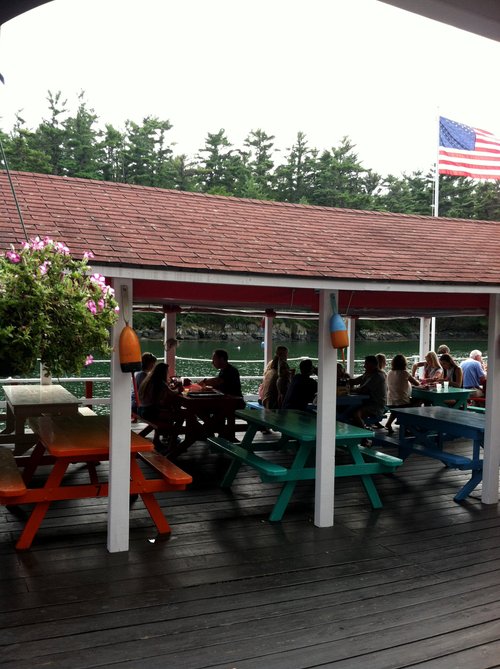 Diners at picnic tables on a covered waterside deck
