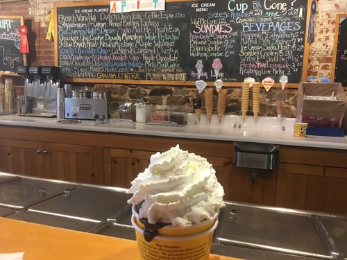 Ice cream with whipped cream at a parlor counter, menu board behind