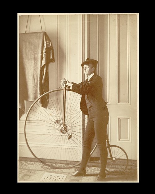 Woman in a suit standing beside a high-wheel bicycle