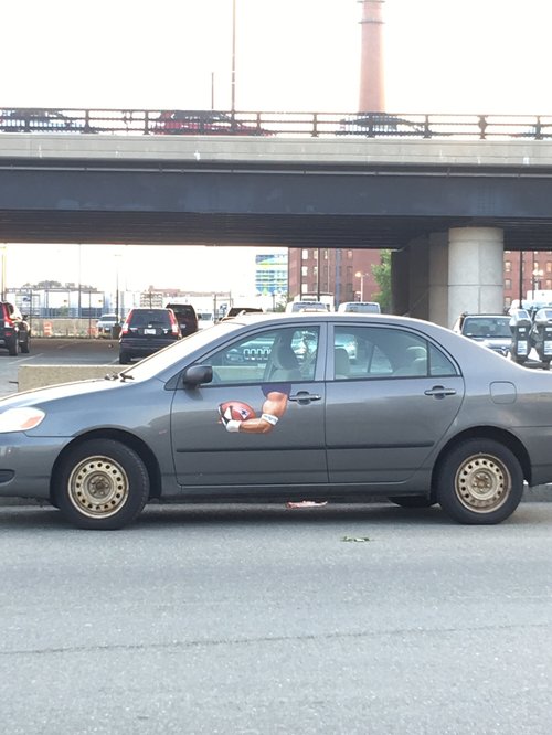 Grey sedan with a small toy figure stuck to its door